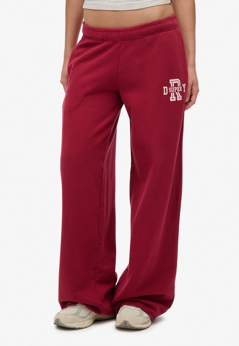 Bordeaux wijdvallende sweatpants met een elastische tailleband, voorzien van een wit logo aan de linkerkant. Gemaakt van zachte, comfortabele stof.
