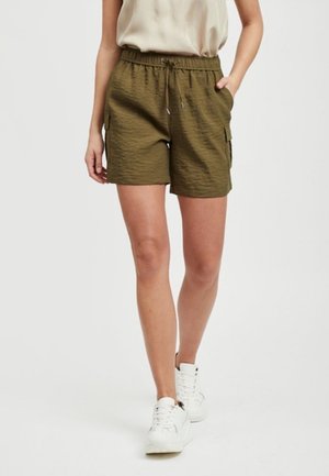 Shorts cargo vert olive avec une taille élastique, des poches latérales et un tissu texturé. Associés à des baskets blanches.