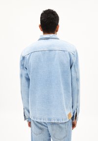 Lichtblauwe spijkerjack met een relaxed fit, contrasterende stiksels en een patchdetail bij de zoom. Heeft lange mouwen en een omgeslagen kraag.