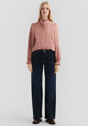 Rose-colored blouse with pleated detailing, button front, and ruffled cuffs. Paired with dark blue straight-leg jeans and brown shoes.