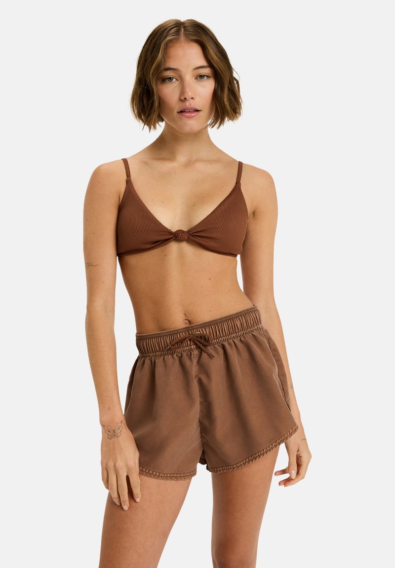 Braun geripptes Bralette mit Knoten-Detail und verstellbaren Trägern, kombiniert mit locker sitzenden braunen Shorts mit elastischem Bund.