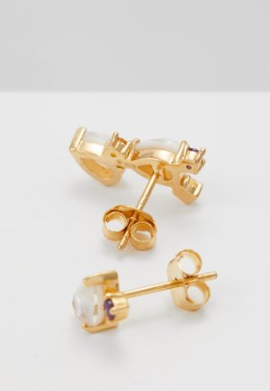 Par af guldørestikker med klare ædelsten sat i kloindfatninger på en hvid overflade.