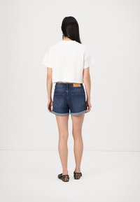 Valkoinen lyhythihainen cropped t-paita yhdistettynä tummansinisiin farkkushortsihin, joissa on käännetyt lahkeet ja takataskut, päällä leopardikuosiset ballerinat.