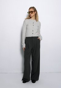 Jasnoszare, zapinane kardigany z miękkiego materiału. Połączone z ciemnymi, szerokimi spodniami z przodu z fałdami. Duże żółte okulary przeciwsłoneczne.