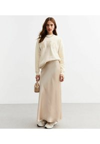 Krämsvettröja med "NYC" tryck, i kombination med en flödande beige maxkjol och vita chunky sneakers. Håller en liten beige handväska.