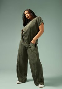 Olivgrön, veckad topp med korta ärmar och löst sittande, vida byxor. Har sidofickor och vita sneakers.