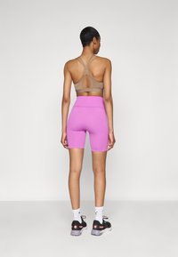 Soutien-gorge de sport marron avec un détail au dos en clé, associé à un short de cyclisme rose et des chaussures de sport noires avec des accents roses. Chaussettes blanches à crew.