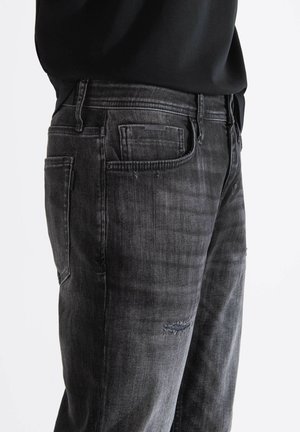 Zwarte denim jeans met een versleten uitstraling, voorzien van een klassiek vijf-pocket ontwerp en subtiele vervaging, inclusief een klein beschadigd gebied.