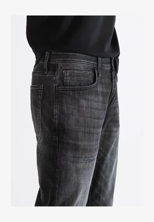 Crne traperice od denima s istrošenom teksturom, koje imaju klasičan kroj s pet džepova i blago izblijedjelim dijelovima, uključujući mali područje s oštećenjem.