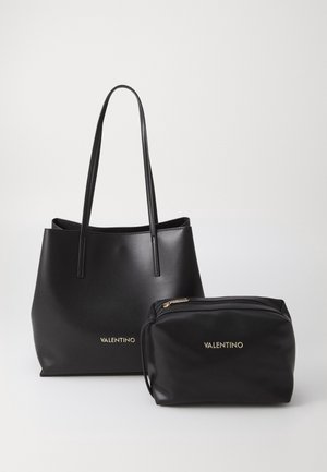 Sac cabas en cuir noir Valentino avec longues anses et pochette noire assortie zippée avec logos dorés sur un fond neutre.