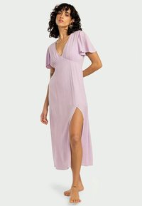 Vestido lavanda, até ao joelho, em tecido canelado, com um decote em V profundo, mangas soltas e uma fenda lateral para maior mobilidade.