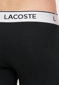 Fekete pamut boxer alsónemű fehér derékrésszel, amelyen fekete "LACOSTE" logó található. Simább textúrájú, testhezálló kialakítás, minimalista stílus.