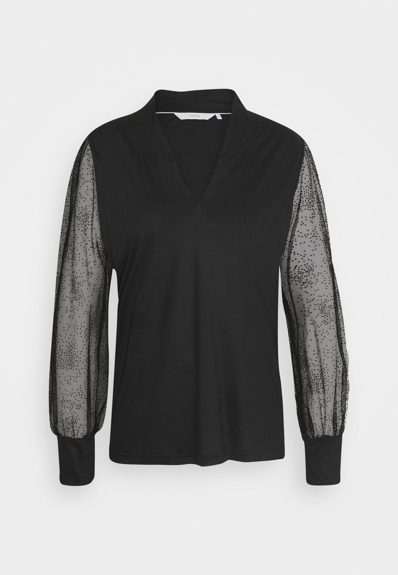 Blouse noire à manches longues avec manches en maille transparente à pois, col en V profond et poignets unis sur fond blanc uni.