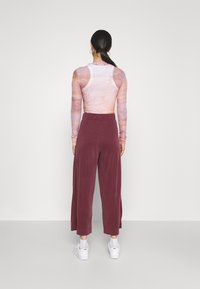 Langarmshirt met een gradientpatroon in zachte tinten, gecombineerd met losse bordeauxrode broeken en witte sneakers. Zachte textuur overal.