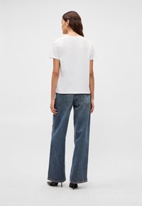 Hvit kortermet T-skjorte kombinert med løse blå jeans i denim. Enkelt design, avslappet passform og diskré sømmer på lommene.