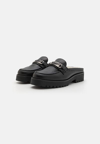 Black leather clogs with a rounded toe, thick rubber sole, and decorative metal hardware across the instep. Smooth texture with stitching accents.