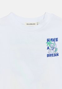 Λευκό βαμβακερό t-shirt με πολύχρωμο γραφικό και κείμενο "ΚΑΝΕ ΜΙΑ ΠΑΥΣΗ" και μια εικονογράφηση χαρακτήρα με φύλλα φοίνικα.