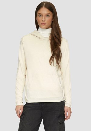Crème hoodie met een voorzak, losse fit en koordkap, gedragen over een witte coltrui. Gecombineerd met donkere cargobroeken.