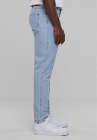 Jeans in denim azzurro con taglio dritto, caratterizzati da legggeri segni di usura sulla tasca posteriore e abbinati a sneakers bianche.
