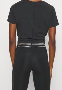 Camiseta corta negra con corte recto y detalle de costura en la parte posterior, combinada con leggins negros que tienen una cinturilla elegante con acentos reflectantes.