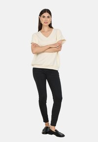 Cream-colored V-neck top with short sleeves, paired with black skinny pants and black loafers, displayed on a neutral background.