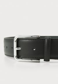 Curea din piele neagră cu o cataramă argintie strălucitoare, având găuri pentru ajustare și o textură netedă. Design minimalist și accesorii funcționale.