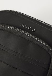 Černá nylonová taška s kovovým zipem a logem ALDO. Materiál má hladkou texturu a zesílené švy.