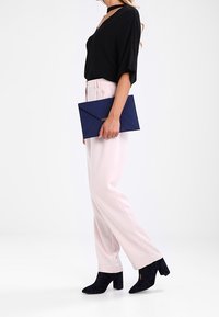 Top nero a coste, pantaloni rosa chiaro, clutch blu navy; stivali neri con tacco e texture. Attenzione al design elegante e alla combinazione cromatica complementare.