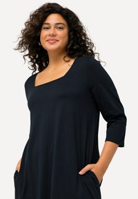 Dunkelblaues Kleid mit quadrischem Ausschnitt, Dreiviertelärmeln, weitem Schnitt und seitlichen Taschen, aus weichem, fließendem Stoff gefertigt.