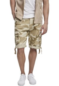 Beige camouflagemönstrade cargoshorts med flera fickor, dragsko i nederkant och en avslappnad passform, tillverkade av andningsbart material. Bärs med vita sneakers.