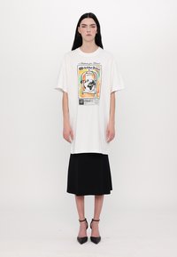 Hvit oversized T-skjorte med et fargerikt grafisk design av en hund i et bur. Kombinert med et elegant svart knelengde skjørt og svarte hæler.