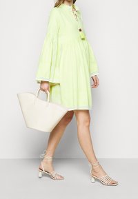 Světle zelené šaty s roztomilými rukávy, strukturovaná tkanina, výstřih do V a detaily s třásněmi. V kombinaci s béžovou taškou na rukojeti a sandály na podpatku.