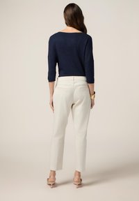 Top en tricot bleu marine à manches trois-quarts, avec des accents scintillants. Associé à un pantalon crème et des sandales à talons nude, vu de dos.