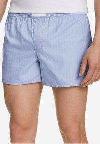 Shorts bleu clair en tissu doux et lisse. Ils disposent d'une ceinture élastique et d'une poche arrière avec un détail de couture subtile.