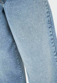 Jeans in denim azzurro chiaro con un motivo a pois, arricchiti da piccole decorazioni bianche. Taglio standard e cuciture visibili.