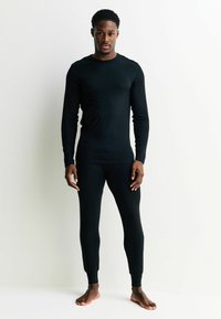 Čierne tričko s dlhými rukávmi a priliehavé legíny, oba vyrobené z hladkého, elastického materiálu. Navrhnuté pre pohodlie s elegantným, minimalistickým strihom.