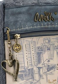 Accesorio de moda con un exterior texturizado en color marino, una sección de lona clara con bocetos impresos y acentos en tono dorado, incluyendo un charm en forma de corazón.