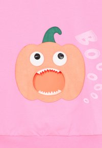 Sweatshirt rosa com um aplique de abóbora laranja, com um caule verde, olhos grandes e uma boca aberta a mostrar dentes, com o gráfico "Boo!".