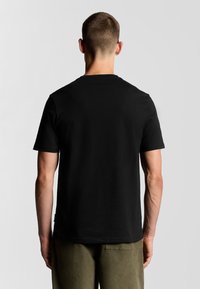 Camiseta negra de manga corta con cuello redondo, hecha de algodón, con un diseño liso y un corte holgado. Se lleva con pantalones verde oliva.