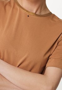 Camiseta marrón con una textura suave y un cuello metálico dorado. Mangas cortas, diseño sencillo y un corte relajado.