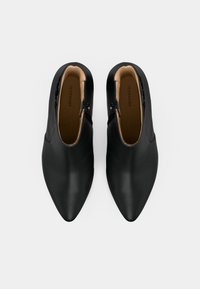 Sapatos pretos de couro com bico apontado e acabamento liso, apresentando um fecho com zíper na lateral e um forro interior em tom bege claro.