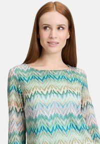Langärmliges Oberteil mit einem Zickzackmuster in Blau-, Grün- und Rosatönen, aus einem leichten Stoff mit glatter Textur gefertigt.