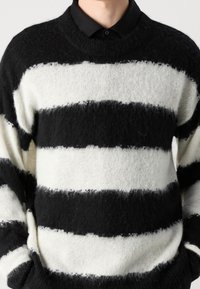 Sweter dziany z wyraźnymi czarno-białymi paskami, z okrągłym dekoltem, o fakturowanym wykończeniu i miękkim, puszystym wyglądzie.