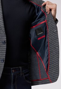 Grau Hahnentritt-blazer mit navy-farbenem Futter, roten Akzenten und einer sicheren Innentasche. Sichtbare Knopfverschlüsse.