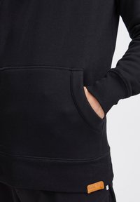Sudadera de algodón negra con un bolsillo delantero, puños acanalados y un dobladillo, con una pequeña etiqueta color beige para la marca.