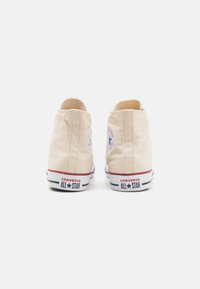 Beige canvas hoge sneakers met witte rubberen zolen, voorzien van rode en blauwe accenten, en het klassieke All-Star-logo op de hiel.