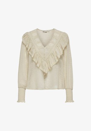 Blusa di colore crema con scollatura a V e bordo in pizzo arricciato. Presenta puntini testurizzati, maniche lunghe con polsini arricciati e chiusura a bottoni.