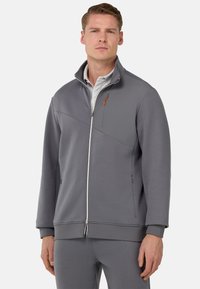 Veste zippée grise avec col montant et panneau contrastant. Comprend des coutures visibles, des poches latérales et un accent orange subtil sur la fermeture éclair.