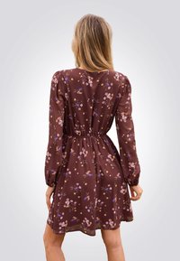 Braunblumenkleid mit langen, gepufften Ärmeln, gerafftem Bund und schwingendem Rock. Es zeigt kleine, mehrfarbige Blumenmuster.