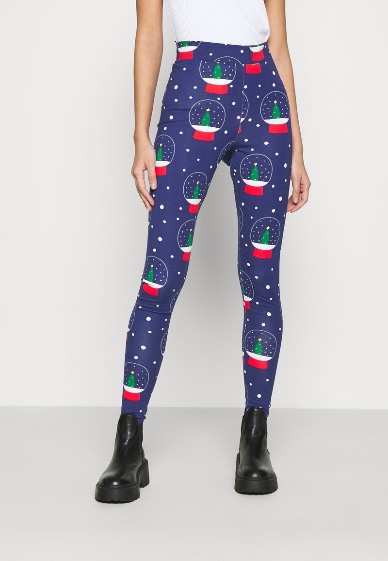 Navy leggings with snow globe and tree pattern, featuring red accents and white dots. Stretchy fabric with a high waist design. Black ankle boots.